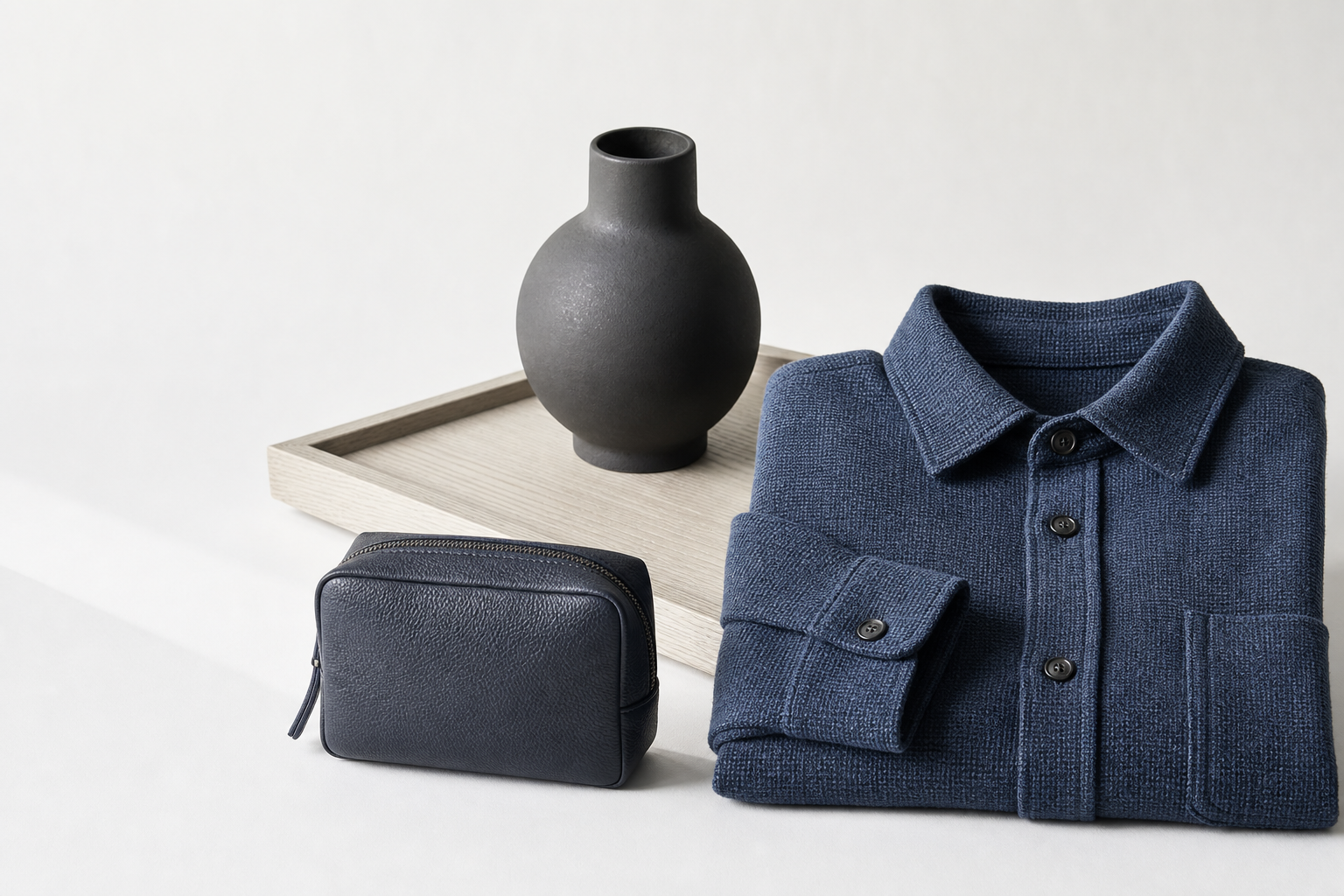 A woven overshirt, leather pouch, ceramic vase, and wood tray
